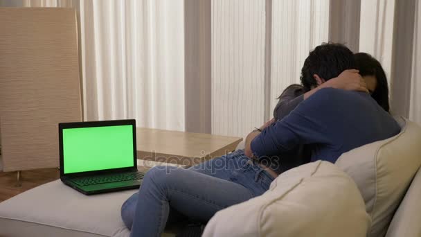 Pareja casada viendo una película de suspenso en la sala de estar, habitación en un ordenador portátil con pantalla verde abrazando y riendo — Vídeos de Stock