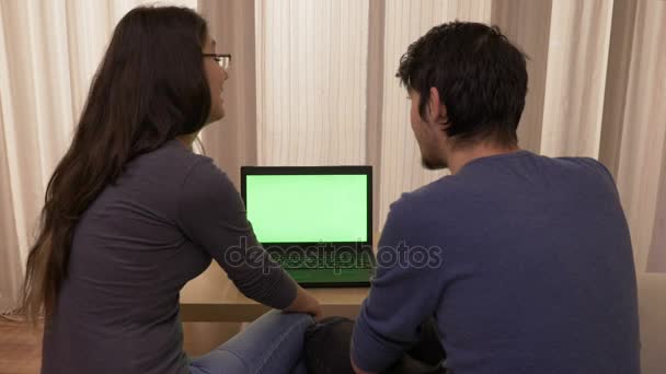 坐在家里沙发上的年轻学生使用带有绿色屏幕的笔记本电脑讨论和比较互联网上的价格 — 图库视频影像