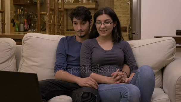 Atractiva pareja joven y cariñosa viendo películas en el portátil en casa en la sala de estar en un sofá blanco — Vídeos de Stock