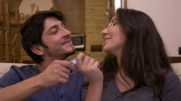 快乐的年轻夫妇笑着争夺信用卡, 在家里的沙发上接吻 — 图库视频影像