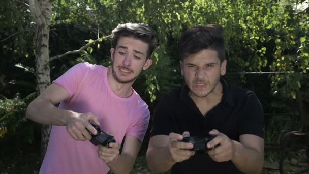 Competidores jóvenes enfocados jugando un concurso de videojuegos usando joystick outdoor en la naturaleza — Vídeos de Stock
