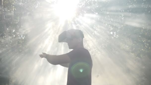 Захоплений тисячоліттям одягнений в окуляри віртуальної реальності VR гарнітура відчувається вражений візуальним досвідом вивчення кіберпростору природа і сонце в диму повільний рух — стокове відео