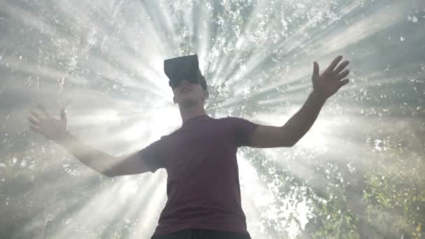 Young man with VR headset gadget immersed into virtual reality covered by light rays and waving smoke in slow motion — Stock Video