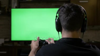 Bağımlılık genç video oyun kumandasını kullanarak yeşil ekranda Tv evde oyun oynarken ve tüyler ürpertici Kulaklık takmış