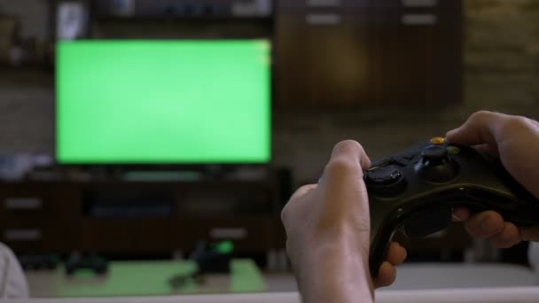Мужские руки, держащие геймпад перед хрома ключ зеленый экран плазменный дисплей, играющий в видеоигры на консоли — стоковое видео