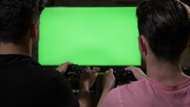 Competitive male friends enjoy playing video games with controllers watching at chroma key TV green screen at home — Stock Video