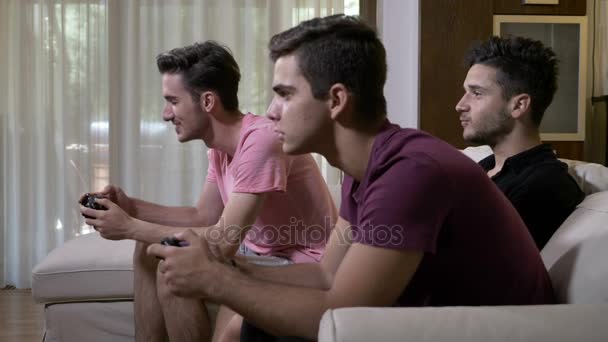 Веселі молоді друзі проводять час вдома, сидячи на дивані, їдять попкорн і грають у відеоігри на консолі — стокове відео