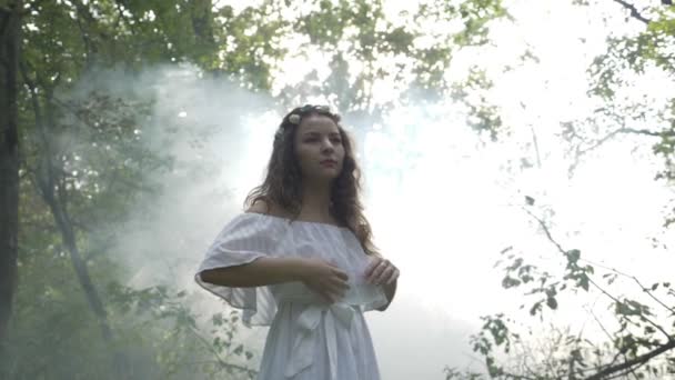Menina angelical misteriosa em vestido branco girando entre as árvores na floresta — Vídeo de Stock