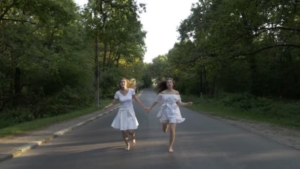 Jeunes femmes attirantes vêtues de blanc courant pieds nus sur une route de campagne forestière tenant la main — Video