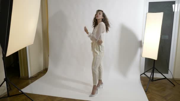 Улыбающаяся известная актриса элегантно одетая в белое позирует в студии с руками в кармане и волосами с одной стороны для фотографа — стоковое видео