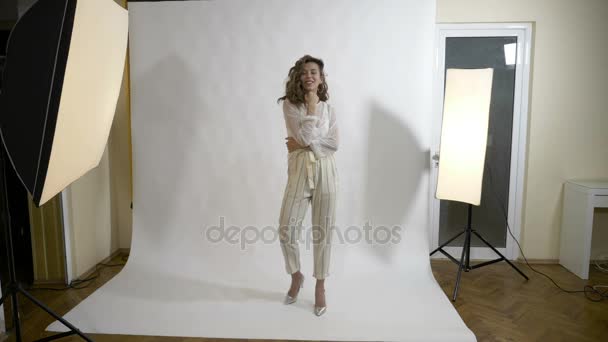 Привлекательная молодая модель с длинными волосами позирует в профессиональной студии с белым фоном для студенческого фотографа — стоковое видео