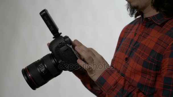 Fiatal férfi fotós szakáll ellenőrzése és törlés a fényképeket, hogy ő tette a fehér stúdióban a profi dslr fényképezőgép — Stock videók