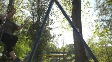 Çekici genç kadın modeli giyiyor spor giyim ve having fun yalnız doğa Park yavaş çekimde bir salıncak üzerinde