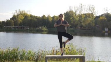 Meditasyon ve yoga yaparken genç ince kadın ağır çekimde iç barış bulmak için bir parkta tek ayak üzerinde duran teşkil etmektedir.