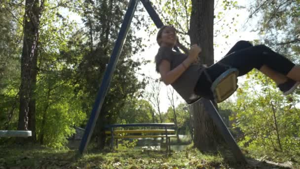 Fit happy female with long and toned legs wearing sport shoes swinging in park on a summer day in slow motion — Stock Video