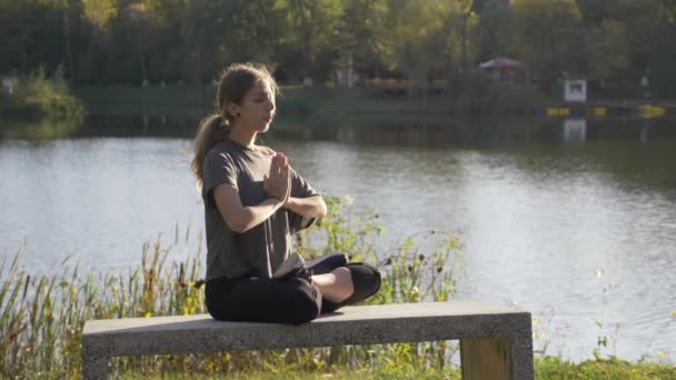 Beautiful young student girl doing yoga outdoor in nature and meditating in lotus position one day before her exams in slow motion — Stock Video
