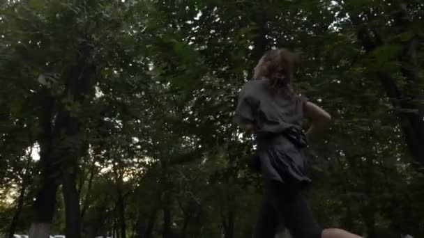 Bella ragazza con i capelli lunghi arricciati che corrono vicino agli alberi nel parco per perdere peso extra al rallentatore — Video Stock