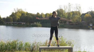 Güneşli bir yaz göl yakınındaki doğada yoga yaparken kıvrılmış saçlı aktif kadın modeli