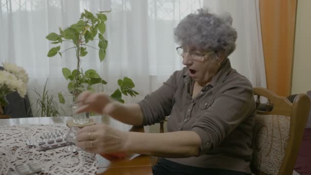 Γέρων γυναίκα τακτοποίηση της φαρμάκου σε ένα χάπι πλαίσιο οργάνωσης και ρίχνοντας μία κάψουλα το τραπέζι στο σαλόνι — Αρχείο Βίντεο