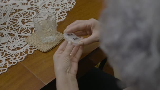 Ältere Frau nimmt ihre Morgenmedikamente aus einem Zeitpillenplaner und trinkt Wasser — Stockvideo