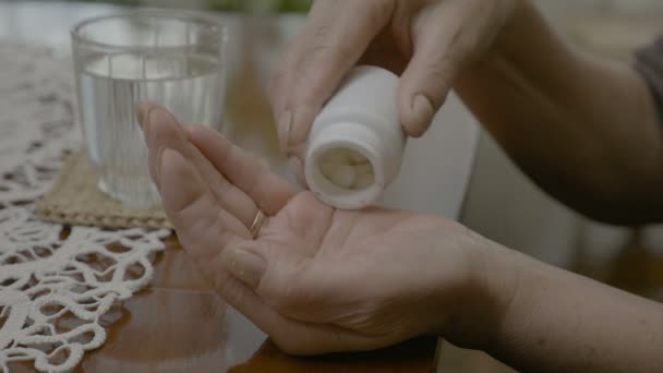 Руки літньої жінки спорожнюють пляшку таблеток у долоні, тримаючи і ковтаючи їх — стокове відео