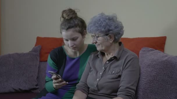 Abuela y nieta sentadas en el sofá y mirando fotos de vacaciones en el teléfono inteligente — Vídeos de Stock