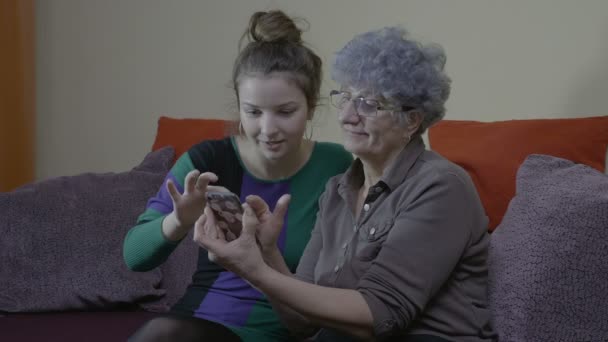Unokája látogató és tanítás nagyanyja, hogyan kell használni az új okostelefon otthon a kanapén — Stock videók