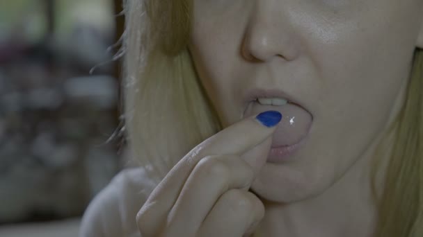 Närbild av en blond smal kvinna att sätta ett vitt litet piller på hennes tunga och svälja det med ett glas vatten — Stockvideo