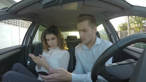 Νεαρό ζευγάρι χρησιμοποιώντας έξυπνα τηλέφωνα αυτοκινήτου και άνθρωπος δείχνει τηλέφωνο την φίλη και είναι σοκαρισμένος — Αρχείο Βίντεο