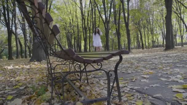 Atractiva mujer vestida con ropa blanca que camina por el parque y pasa los dedos por el pelo en un día de otoño en cámara lenta — Vídeos de Stock