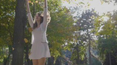 Eğleniyor ve sonbahar yaprakları ile özgürlük zevk ve ağır çekimde güneşli bir parkta iplik çekici ince genç kız