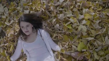 Ağır çekimde parkta güzel model kız gülümseyerek ve sonbahar üzerinde yatan bırakır