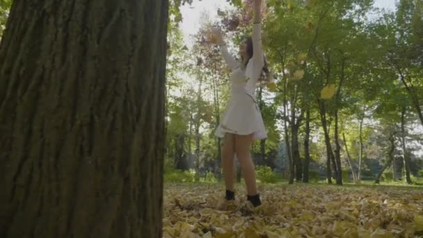 Тонкая европейская девушка наслаждается прекрасным осенним днем и прядется среди падающих желтых листьев дерева в замедленной съемке — стоковое видео