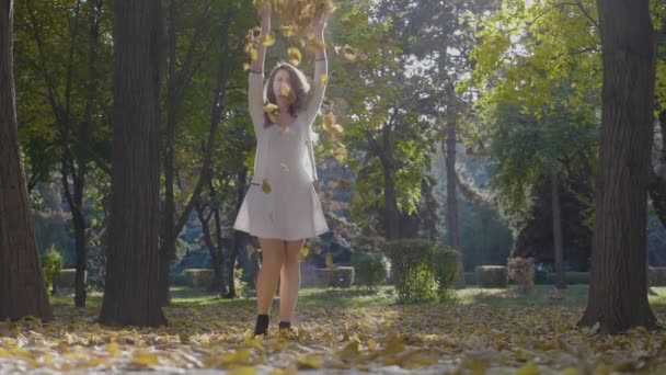 Belle adolescente profitant du week-end dans le parc en ramassant les feuilles d'automne du sol et en les jetant dans les airs au ralenti — Video