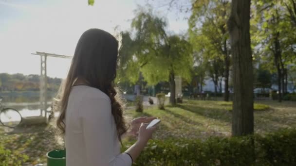 Jovem mulher de negócios bonita com cabelos longos tendo um passeio no parque e usando smartphone em câmera lenta — Vídeo de Stock