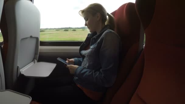 Молода жінка подорожує сама в комфортному поїзді в сільську місцевість, використовуючи свій смартфон — стокове відео