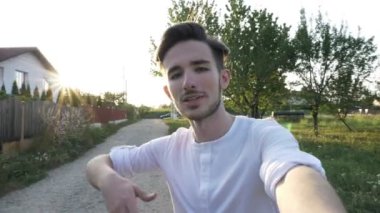 Genç gülümseyen ve el düzenlenen ve kayıt kamera için güneşli bir günde doğa onun blog için video konuşurken adam