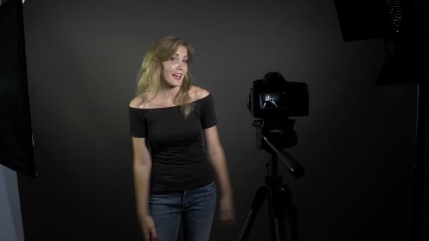 Young smiling blonde female blogger recording vlog message for her subscribers in a professional studio — Stock Video