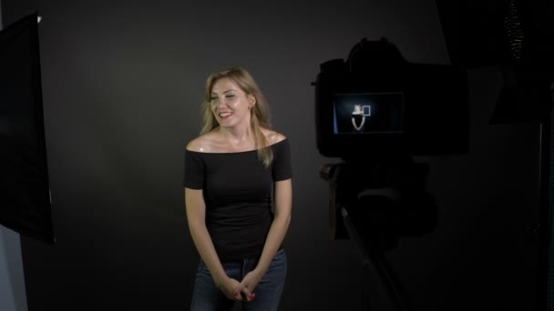 Молодая улыбающаяся счастливая привлекательная девушка снимает для своего видеоблога в профессиональной студии, в то время как бойфренды фотобомба проходит через рамку — стоковое видео