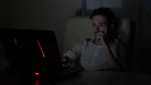 Jonge doordachte ondernemer man zitten in zijn stoel van het Bureau laat in de avond en met behulp van zijn laptop op zoek naar clients op het internet — Stockvideo