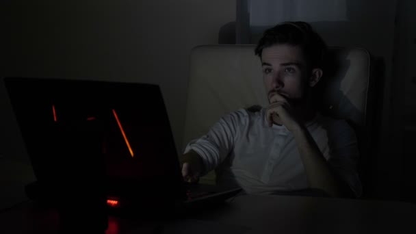 Aantrekkelijke jonge zakenman controleren van online informatie over zijn laptop voor zijn bedrijf laat op de avond in een donkere kamer thuis — Stockvideo