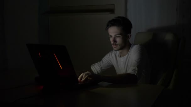 Joven hombre de negocios cansado sentado en su escritorio y trabajando en línea desde su computadora portátil en casa tarde en la noche — Vídeos de Stock