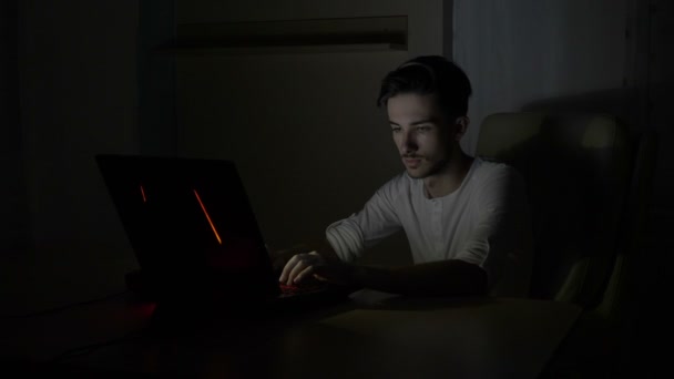 Young male student sitting on his desk at home thinking and solving math problems online on his laptop at night — Stock Video