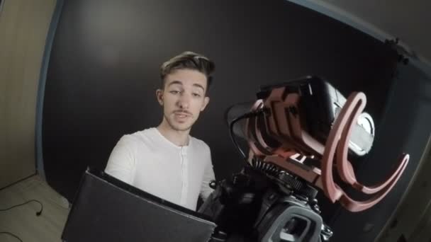 Vlogger laki-laki memegang kamera dengan tangannya dan merekam testimonial di sebuah studio profesional tentang pengalaman liburan terakhirnya — Stok Video