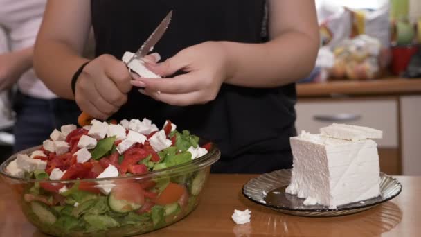 Le mani femminili cucinano aggiungendo formaggio a gustosa insalata sana preparata in ciotola mentre i suoi amici si riuniscono sullo sfondo in cucina. — Video Stock