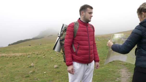 Jeunes touristes drôles perdus couple en voyage d'aventure en montagne étudier ensemble la carte soufflé par le vent — Video