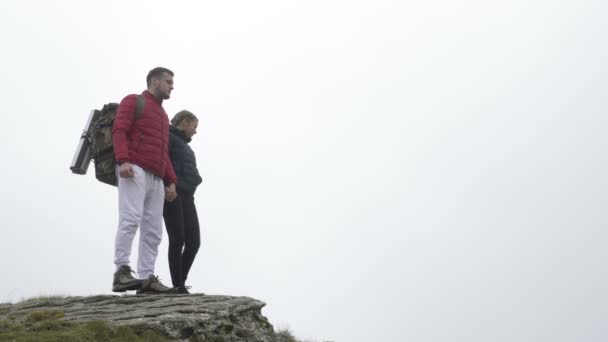 Leistungskonzept mit sportlichem verliebten Paar, das beim Erreichen des Berggipfels jubelnd die Hände hebt und sich küsst und die Aussicht genießt — Stockvideo