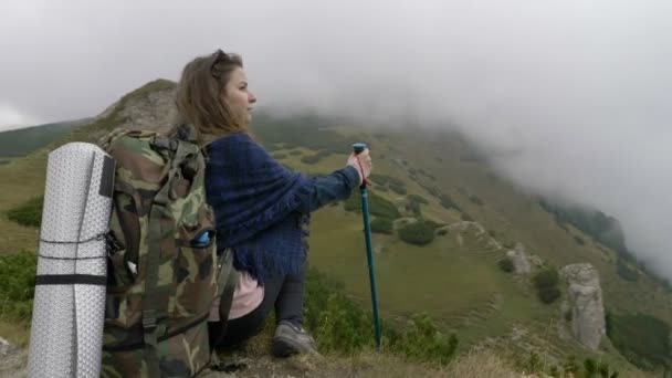 Duizendjarige vrouw op berg excursie staan hoog op de klif op zoek naar het verre prachtige landschap met pieken van de mistige heuvels en bossen — Stockvideo