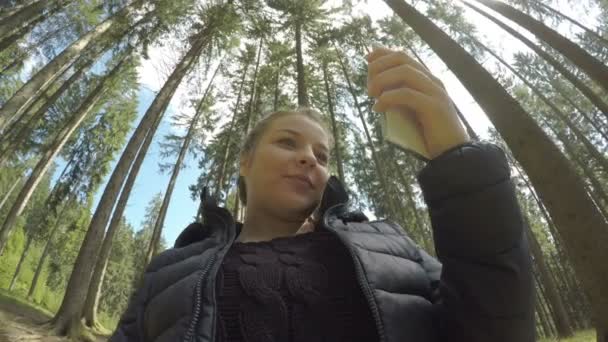 Chica adolescente divertida tomando selfies con teléfono inteligente en un bosque descansando después de senderismo de montaña 360 vista de madera en el fondo — Vídeo de stock