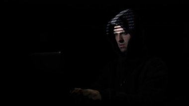 Karanlık bir odada oturuyor ve yüzünde kod karakterlerini yansıtan iken blockchain sunucuları saldıran hood erkek siber suç